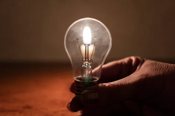 Kesinti. Altyapı tahribatı. Enerji krizi. Elektrik kesintisi konsepti. Yanan bir mum ışığında elinde bir ampul. Yakın plan.