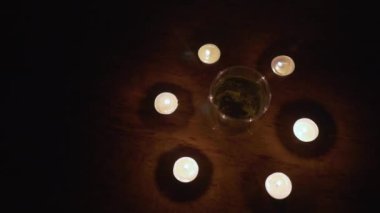 Kesinti. Enerji krizi. Altyapı tahribatı. Elektrik kesintisi konsepti. Şeffaf bir fincan bitki çayı yanan mum çemberinin içinde duruyor. Panorama (kamera soldan sağa hareket eder)