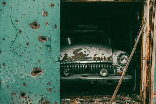 A broken civilian vintage car is in the garage. On the body of the car there are holes from bullets and shrapnel. War in Ukraine. Russian invasion of Ukraine. War crimes