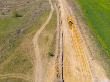 Kırsal kesimde. Bahar. Güneşli bir gün. İnşaat makineleri sahada yeni bir yol açıyor. Drone. Hava görünümü