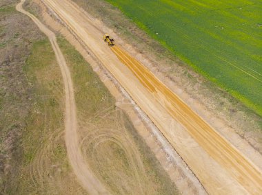 Kırsal kesimde. Bahar. Güneşli bir gün. İnşaat makineleri sahada yeni bir yol açıyor. Drone. Hava görünümü