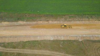 Kırsal kesimde. Bahar. Güneşli bir gün. İnşaat makineleri sahada yeni bir yol açıyor. Drone. Hava görüntüsü. Kamera soldan sağa hareket ediyor.