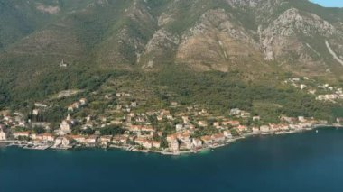 Montenegro. Adriatic Sea. Bay of Kotor. Popular tourist spot. Village on the coast. Houses with orange tiled roofs. Summer. Tourist season. Drone. Fly. Aerial view. The camera moves forward