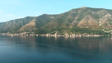 Montenegro. Adriatic Sea. Bay of Kotor. Popular tourist spot. Village on the coast. Houses with orange tiled roofs. Summer. Tourist season. Drone. Fly. Aerial view. The camera moves up