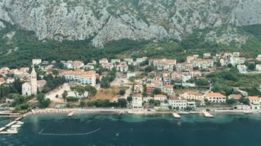 Montenegro. Adriatic Sea. Bay of Kotor. Popular tourist spot. Village on the coast. Houses with orange tiled roofs. Summer. Tourist season. Drone. Fly. Aerial view. The camera moves from left to right