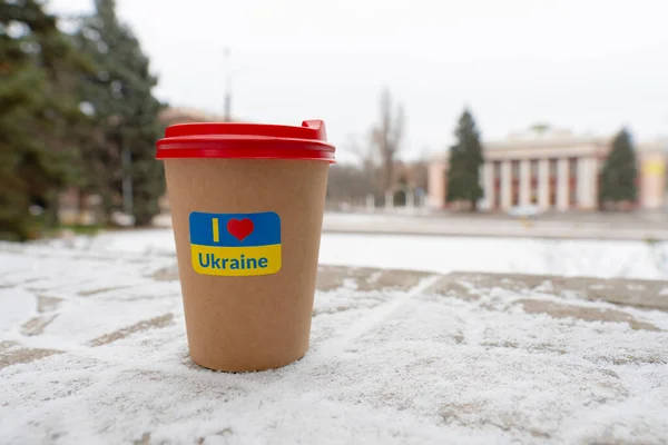 Winter. Cold weather. The ground is covered with a small layer of snow. Cup of coffee with a patriotic sticker \