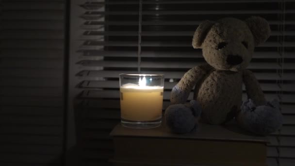 おもちゃ テディベア ろうそくの光によって窓のそばの暗い空の部屋にあります 左から右へ 停電だ エネルギー危機 停電概念 — ストック動画