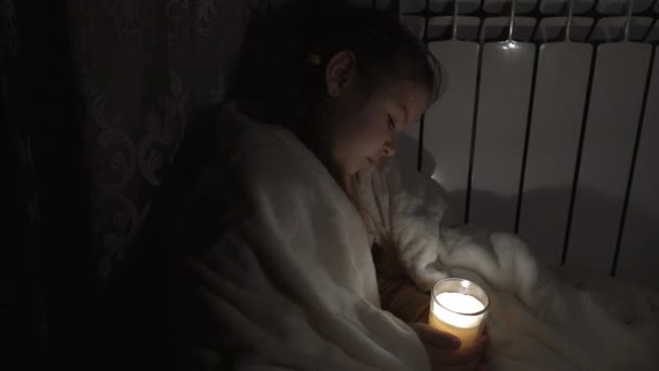一个穿着白色格子花的女孩在一个家用电池的背景下 手里拿着一只玻璃杯里的蜡烛 停电的概念 停电了能源危机 摄像机从左移到右移 — 图库视频影像
