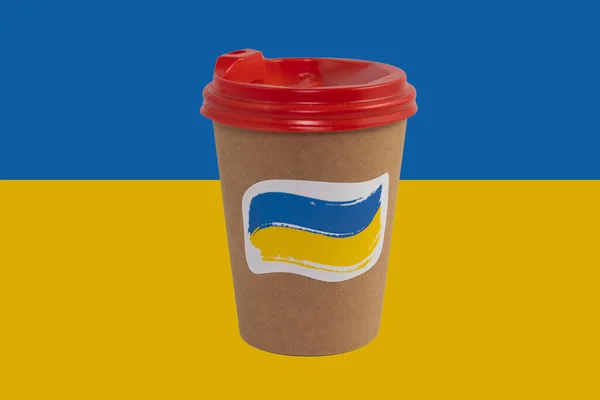 Disposable paper cup of coffee with a patriotic sticker isolated on the background of the national flag of Ukraine (close-up)