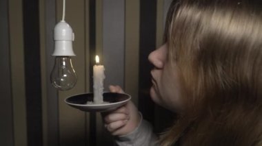 Karanlık bir odada elinde yanan bir mum tutan bir kız elinde bir ampulle bir şamdana bakar (yakın çekim, sabit kamera). Kesinti. Elektrik kesintisi kavramı