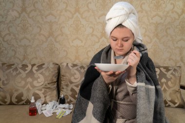 Soğuk belirtileri gösteren bir kız kanepeye oturur ve tabaktan çorba içer. İlaç, sağlık, eczane ve evde tedavi kavramı