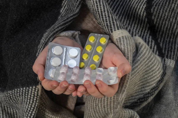 A woman in a plaid holds blisters of pills in her hands (close-up). The concept of medicine, pharmacy, healthcare and treatment at home