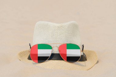 Birleşik Arap Emirlikleri bayrağı şeklinde gözlüklü güneş gözlükleri ve kumların üzerinde duran bir şapka. Birleşik Arap Emirlikleri 'nde yaz tatili, seyahat ve turizm kavramı. Yaz tatili. Tatil sezonu