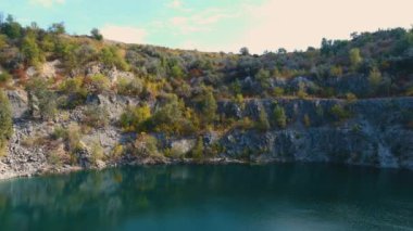 Su basmış ve terk edilmiş granit ocağının temiz turkuaz suyla en üst görüntüsü. Güneşli bir sonbahar günü. Drone (kamera soldan sağa hareket eder)