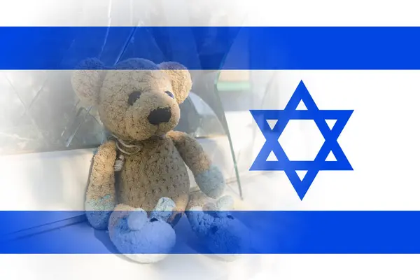 A toy (teddy bear) next to broken glass against the background of the Israeli flag. Israeli-Palestinian conflict. Terror of civilians