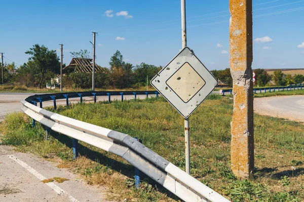 Road sign with bullet holes in a war zone. War in Ukraine. Russian invasion of Ukraine. Countryside. Terror of civilians. War crimes