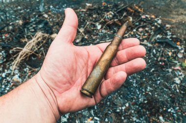 Büyük kalibreli bir makineli tüfek fişeği kömürleşmiş toprağın arka planına karşı. Yakın plan.