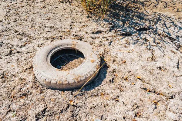 Kuru bir gölün dibindeki çatlamış kil üzerinde eski bir araba lastiği bulunur (yakın plan). İklim değişikliği, kuraklık ve rezervlerin kuruması sorunu kavramı