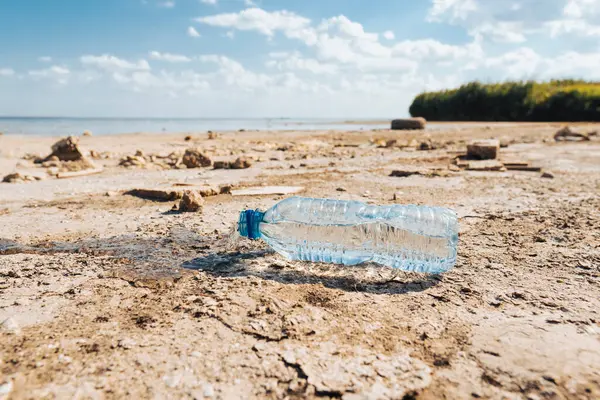 Güneşli bir yaz gününde kurumuş bir gölün dibinde su sızıntısı olan plastik bir şişe yatıyor. İklim değişikliğinin kavramsallaştırılması, su kaynaklarının kuraklığı ve kuruması