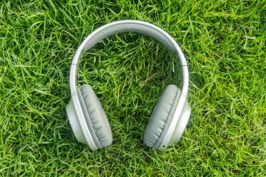 Canlı yeşil çimenlerin üzerinde duran gümüş kulaklıklar, müzik, rahatlama ve açık hava eğlencesi için mükemmel bir görsel.