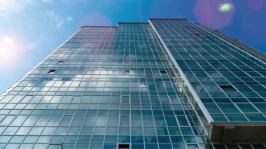 Zaman ayarlı. Mavi gökyüzünde yükselen bulutları yansıtan cam cepheli modern bir ofis binasının alt manzarası.