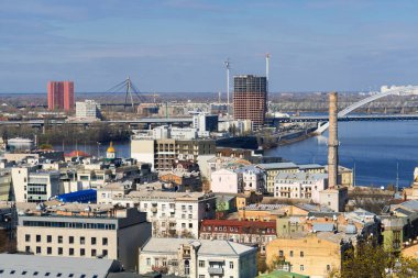 Güneşli bir günde, geniş bir nehir üzerinde eski konut binaları, modern inşaat alanları ve köprülerin karışımı büyük bir şehrin panoramik manzarası.