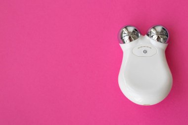 Mikro akım kavramı. Mikro akım yüz masajcısı. Yaşlanmayla savaşmak ve yüzü pembe arka planda sıkmak için kullanılacak bir cihaz. Üst görünüm, düz plan, metin için boşluk