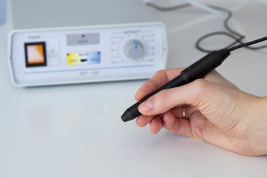 Elektroepilasyon. Doktor elektroepilatör cihazının yanında bir kalem ve iğne tutuyor. Vücut kılları kalıcı olarak alınıyor
