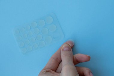 Mavi arka planda, parmağında yuvarlak sivilce ve kırışıklık bantları var. Yüz temizleme kozmetolojisi. Yüz yenileme için sivilce ve kırışıklık bantları.