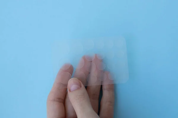 Sticker patches for acne and red spots on the skin in the hand of a girl on a blue background.