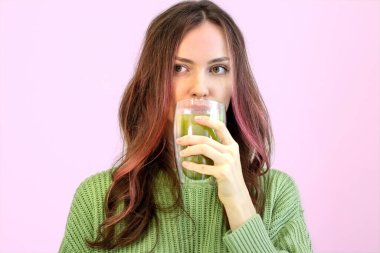 Şık saçlı, kıvırcık saçlı güzel bir kadın pembe arka planda aynı yeşil çayı içiyor.