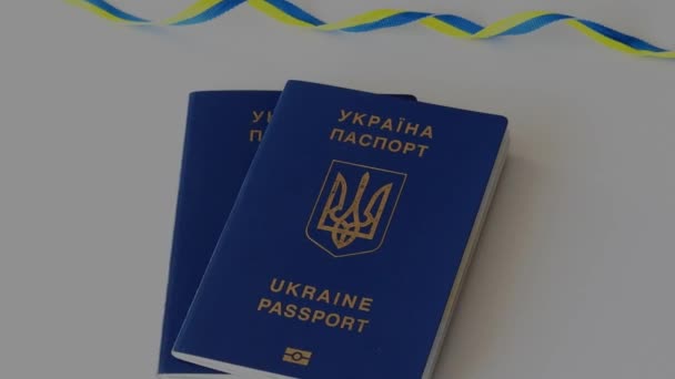 旗の色のリボン付きの白いテーブルの上に2つのウクライナのパスポート — ストック動画
