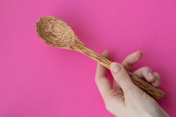 Large wooden spoon in a womans hand on a pink background.