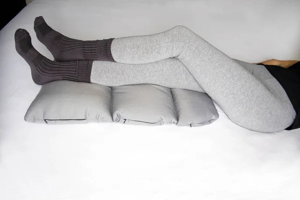 Slim woman rests with her legs up on an orthopedic pillow for vein health and improved circulation