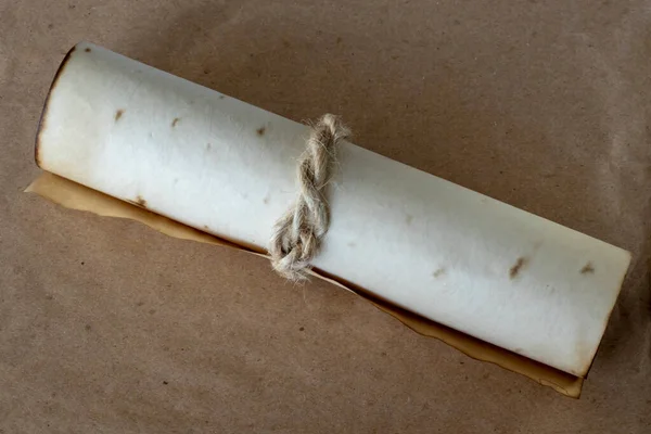 Ancient scroll rolled out of beige paper, tied with a rope on a brown background