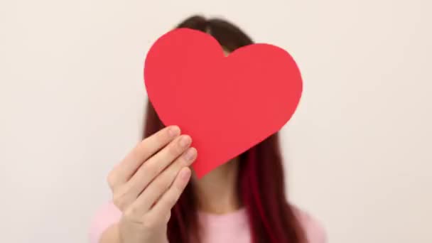 年轻的女人拿着一个红纸心脏 最后用它指向相机 恋爱中的女孩爱情 献血的概念 — 图库视频影像