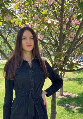 Güzel, siyah kot elbiseli genç bir kadın çiçek açan sakura ağaçlarının arkasında. Pembe çiçekli Sakura. Dikey Fotoğraf.