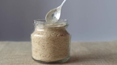 Cam kavanozda besleyici olmayan maya ve kadın elinde kaşık. Yan görünüm. Sarı Besin Taneleri Bir Peynir Yedeği ve Vegan Pişirme İçin Baharat.