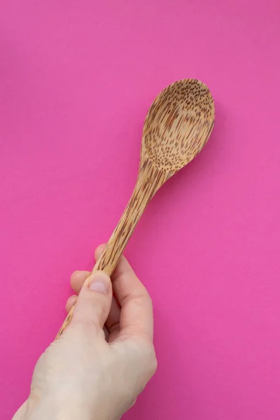 Wooden spoon in the hand of a girl on a pink background.