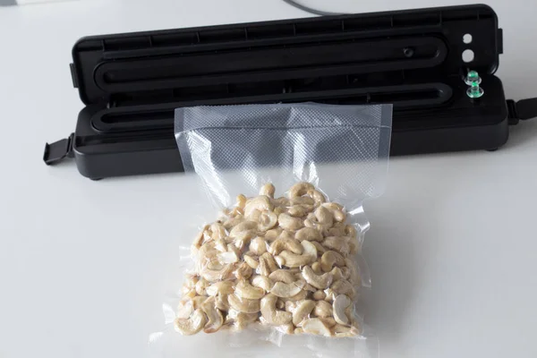 Vacuum packaging machine and vacuum bagged nuts. Device for packing food on a white table with a plastic cashew bag