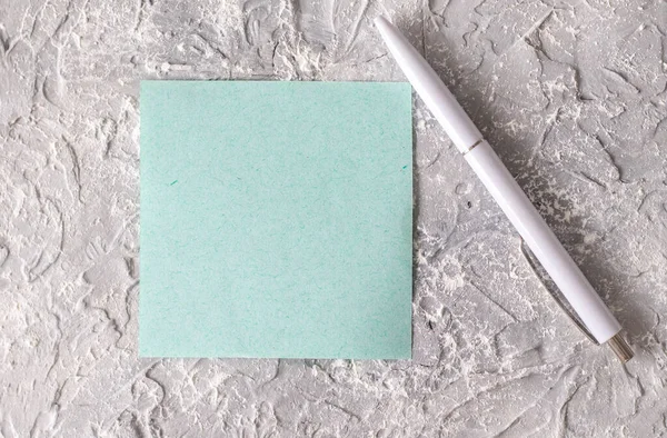Empty square note blue paper on grey textured concrete next to a white pen