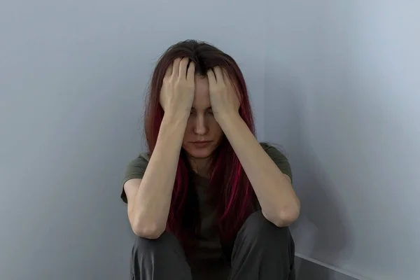 Young woman with mental health problems, depression and ptsd sits in the corner of the room holding her head.