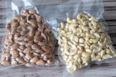 Tahta arka planda kurutulmuş kaju ve badem vakumlanmış. Bitkisel beslenme, sağlıklı yağlar, keto diyeti, lchf. Atıştırmalıklar.