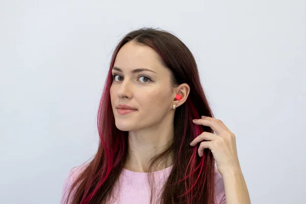 Beautiful young woman with bright pink hair in a pink T-shirt shows her ear with earplugs. Portrait of a woman looking into the camera
