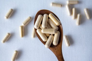 Drug capsule pills with beige medication in pile in a wooden spoon on a white background.