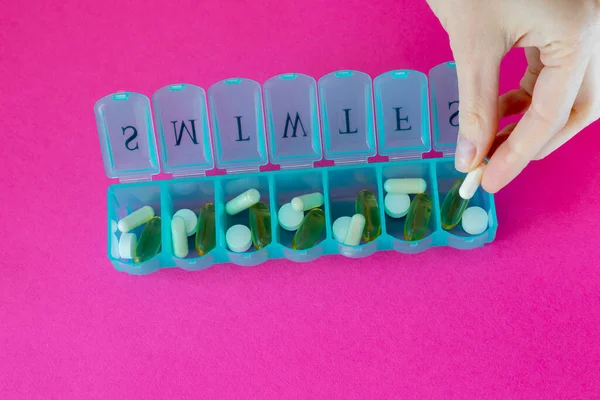 Pill organizer. Various capsules, vitamins and antibiotics in a plastic daily box. The woman fills the cells with tablets