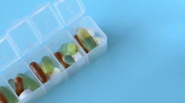 Pill organizer on a blue background. Filled plastic cells with tablets, supplements and vitamins