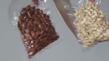 Vacuumed bags of cashews and almonds in womens hands on a white background