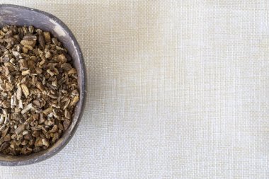 Finely chopped dried burdock root in a natural plate on a linen background. Copy space, top view