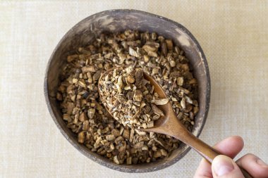 Dried burdock root for making medicinal tea in a wooden spoon on a beige background with a plate